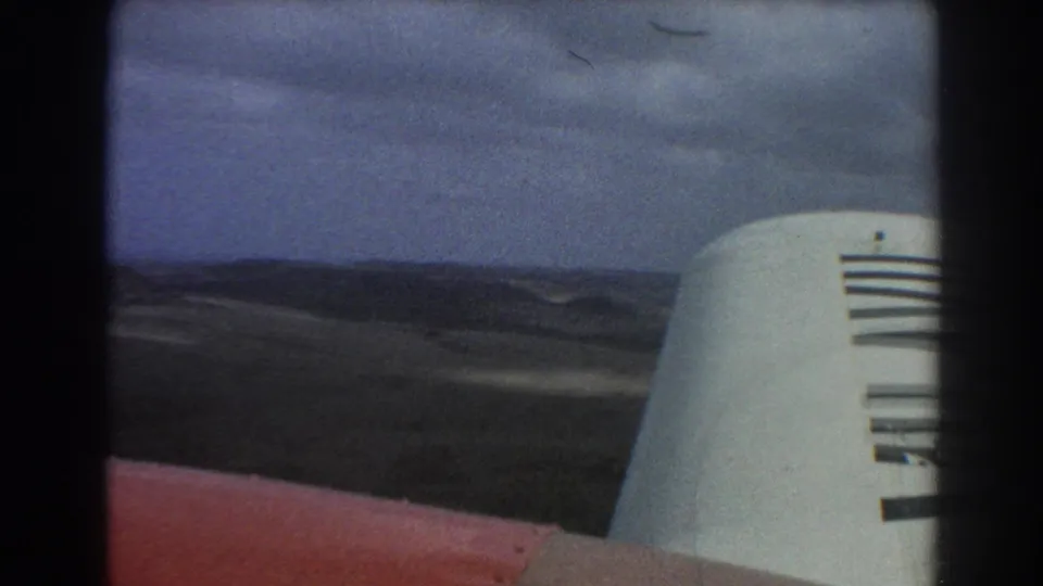 1967 aerial home-movie frame from near Perth showing the aircraft wing and tail fin over dry rolling terrain.