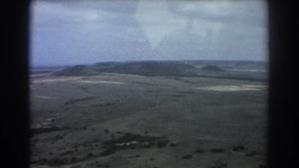 Perth-region 1967 8mm aerial view across open arid ground, distant hills, and softened blue-gray sky.