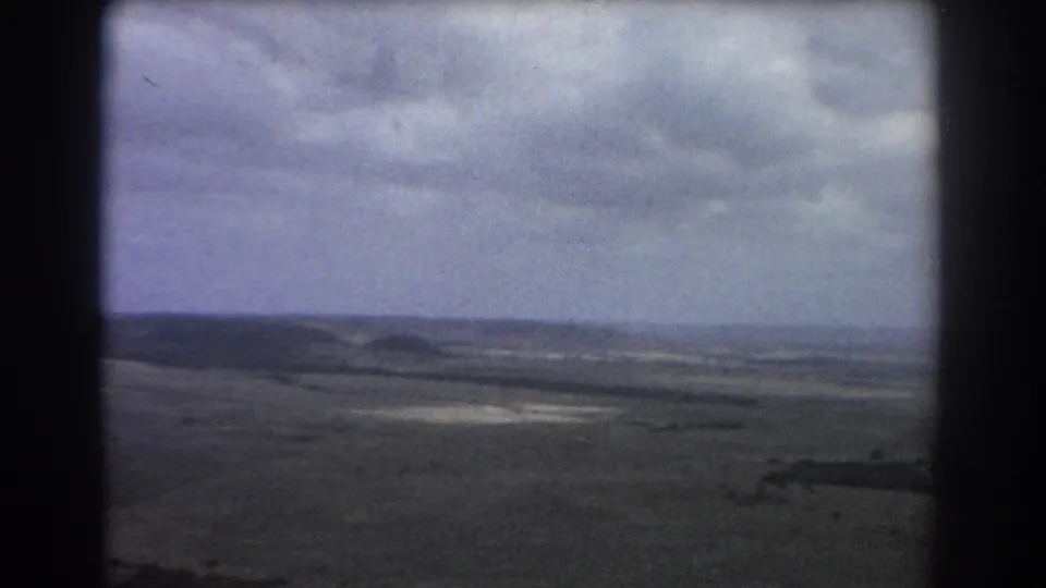 Vintage 8mm aerial frame from the stated Perth, Australia trip, looking across dry terrain and low hills beneath clouds.
