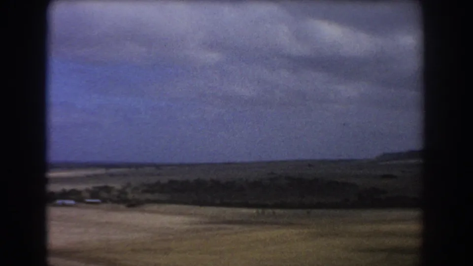 1967 Perth-area home-movie view of pale fields, dark vegetation, distant low hills, and a broad clouded sky.