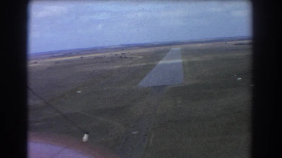 1967 Perth-area aerial view of a long straight runway crossing flat open terrain in grainy 8mm color.