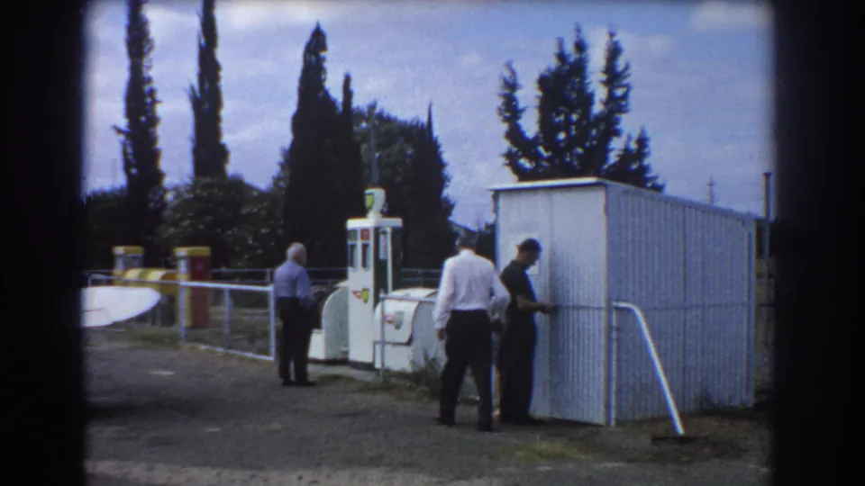 At the Perth airfield, two men stand near the shed door area while another remains beside the white pump.