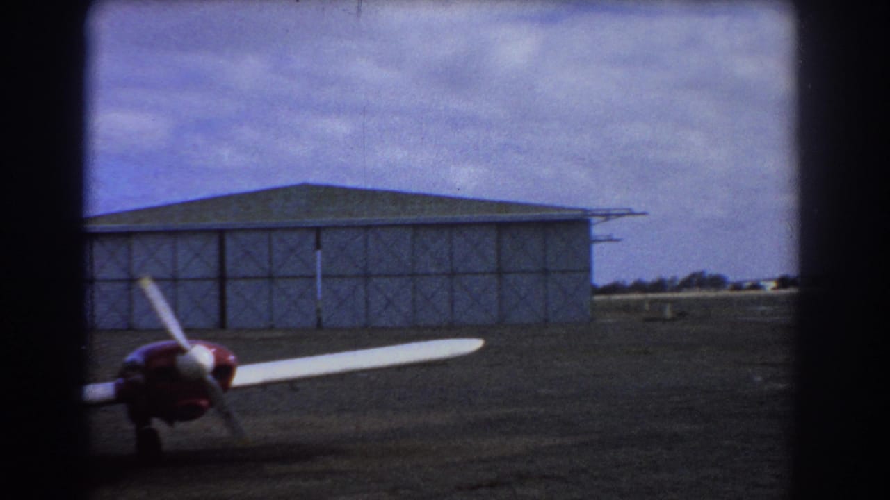Aircraft wing and engine at the edge of a hangar and open airfield.