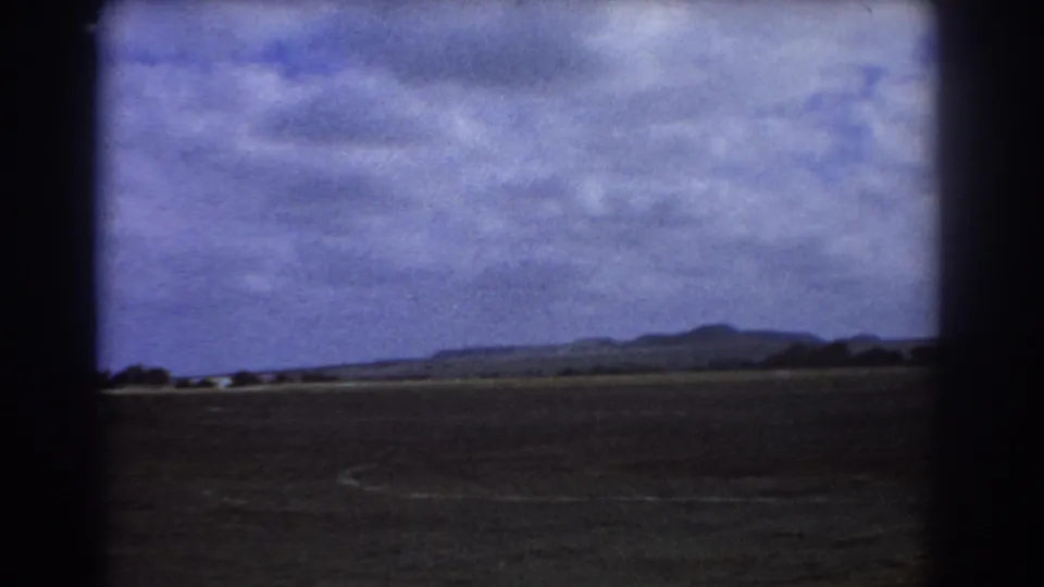 1967 Perth-area aerial view showing flat land, distant hills, cloudy sky, and dark aircraft-window framing on 8mm film.
