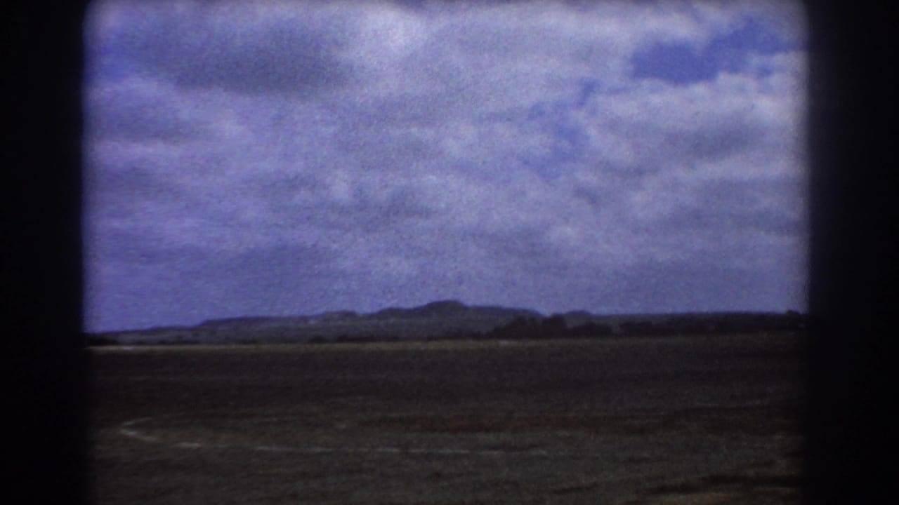 Distant hills and open ground beneath a clouded sky, seen through dark vertical framing.