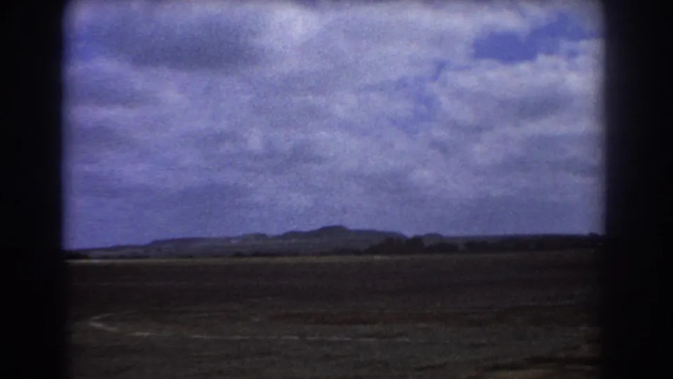 Aerial 8mm view near Perth with distant hills, broad open ground, cloud cover, and dark aircraft-window borders.