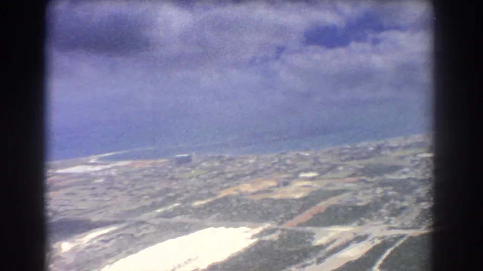 1967 aerial view over Perth showing coastline, surf, roads, scattered buildings, and a bright reflective area below.