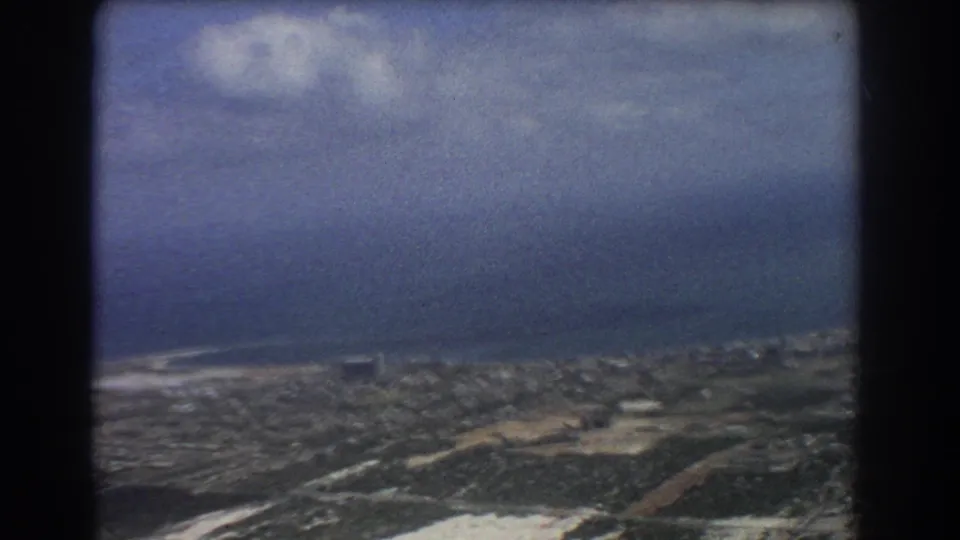 Perth aerial home-movie frame with coastline, low city development, roads, cloud shadow, and dark window framing.