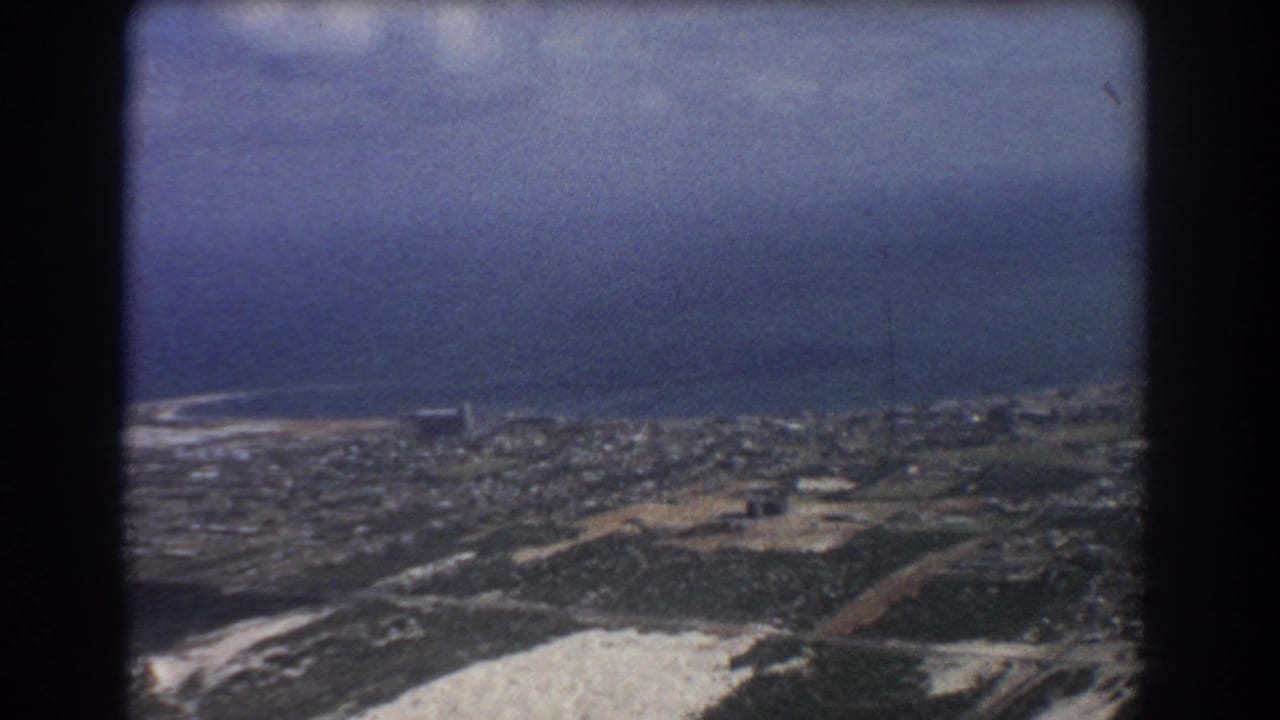 Aerial view of coastal city blocks, open land, and blue ocean through dark film-frame borders.