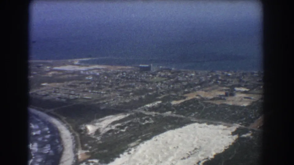 Likely Perth, Australia in 1967, seen from above with ocean, shore, urban spread, open land, and curved aircraft-window framing.