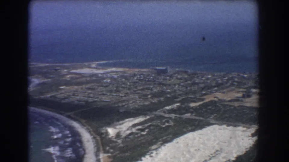 1967 8mm aerial view over Perth coastline with ocean, beach, sandy dunes, roads, and low-rise homes.