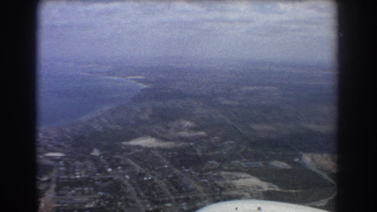 Aerial view over coastal land, streets, waterways, and part of an airplane wing.