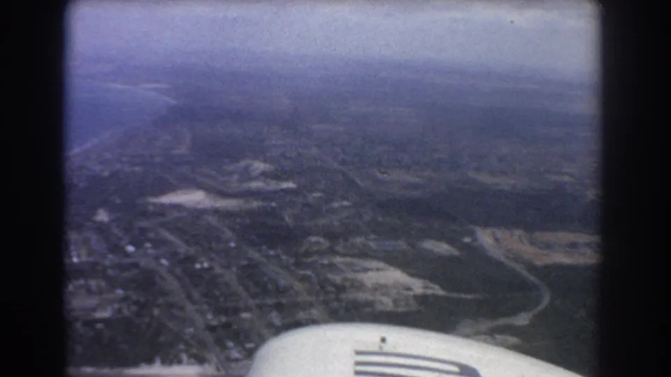 1967 Perth aerial footage shows shoreline, inland water, streets, open areas, and the edge of the aircraft wing in the foreground.