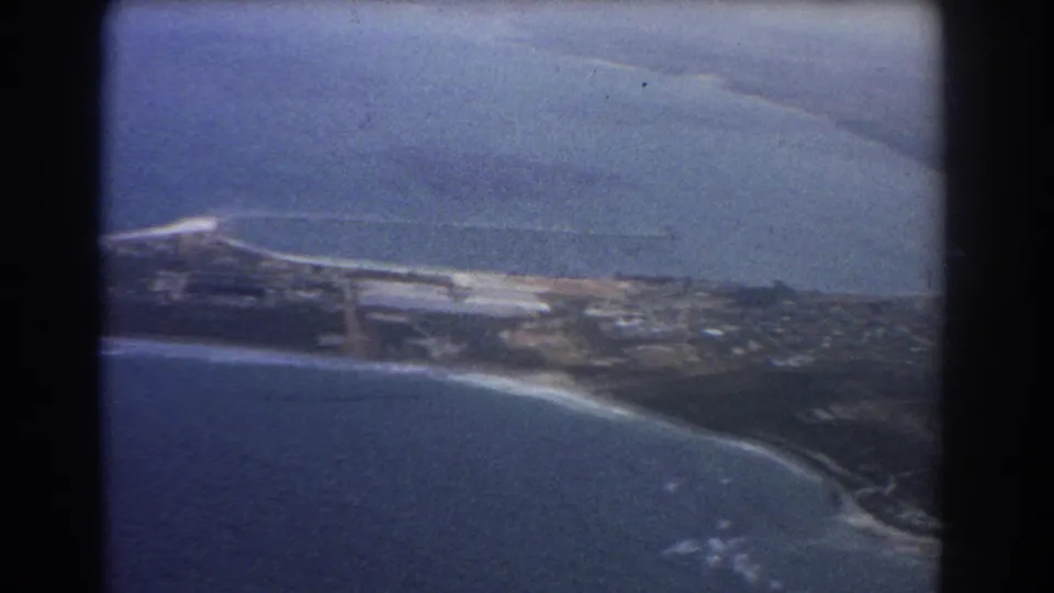 1967 Perth, Australia aerial frame showing a narrow coastal landmass, ocean water, pale surf, and scattered development.