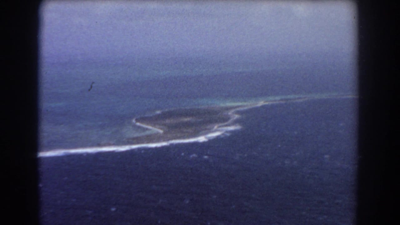 Aerial view of a small island or reef edge surrounded by blue ocean and white surf.
