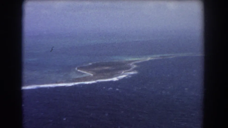 1967 8mm aerial view near Perth, Australia, showing a low island or reef line in blue ocean under hazy sky.