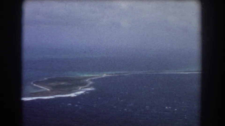 1967 8mm aerial footage near Perth, Australia, with surf tracing a narrow reef or island shoreline across blue water.