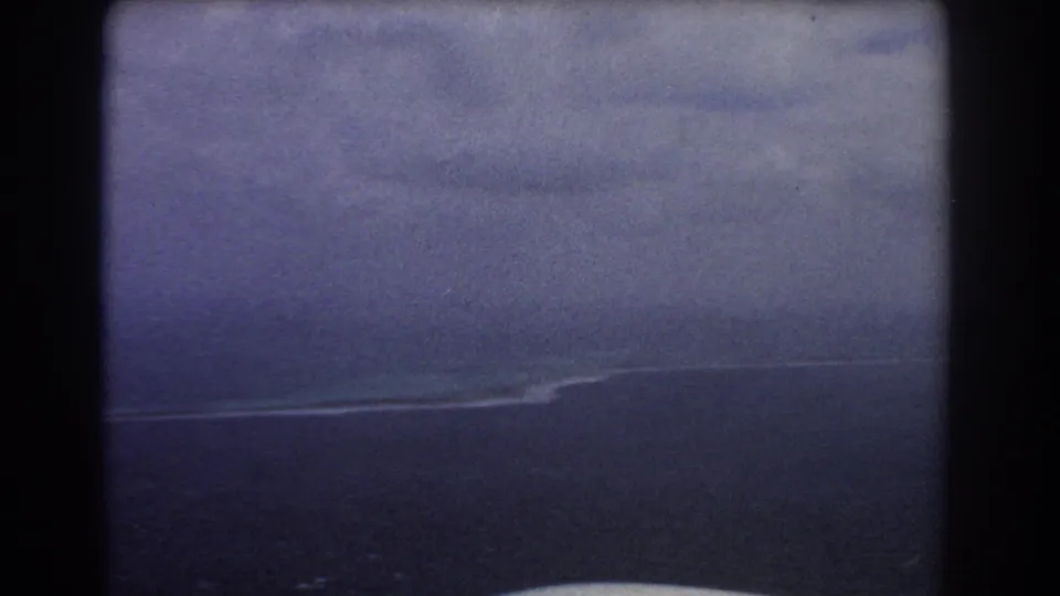 Soft 1967 8mm aerial frame near Perth, Australia, with a faint reef or island edge stretching through blue ocean.