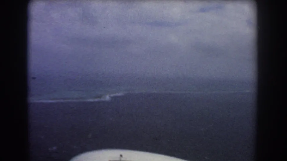 1967 8mm aerial view near Perth with dark ocean, low cloud, distant surf, and the edge of an airplane window visible.