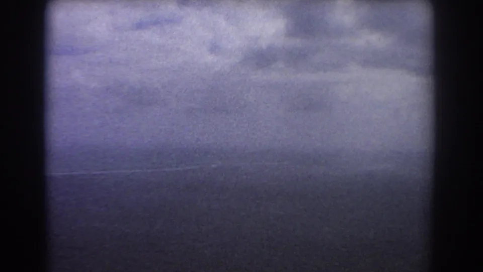 Aerial view near Perth in 1967 with dark ocean, broad cloud cover, faint shore detail, and the soft texture of 8mm film.