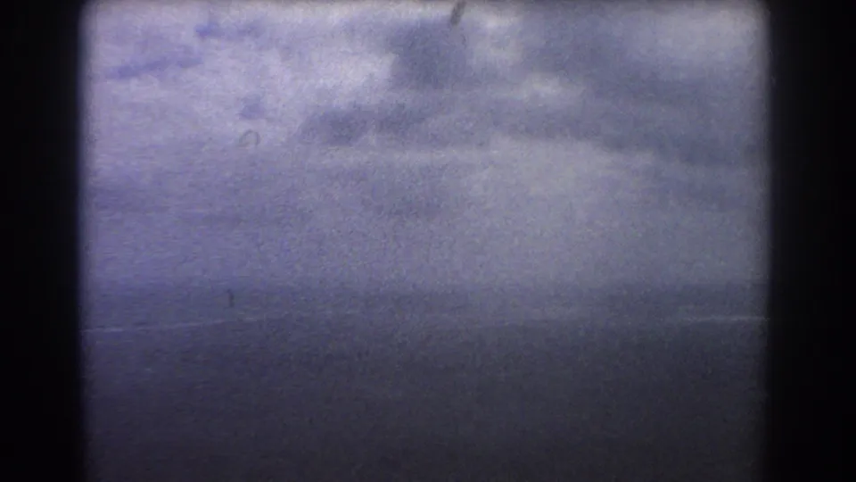 A soft 8mm view from an airplane window shows muted sky and sea before the coastline becomes visible.
