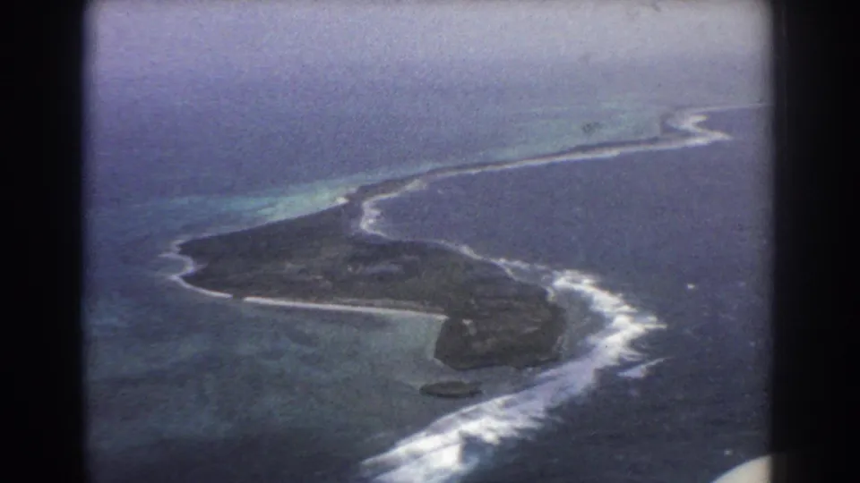 1967 home-movie aerial near Perth, Australia, with an island or reef, white surf, turquoise water and dark airplane-window framing.