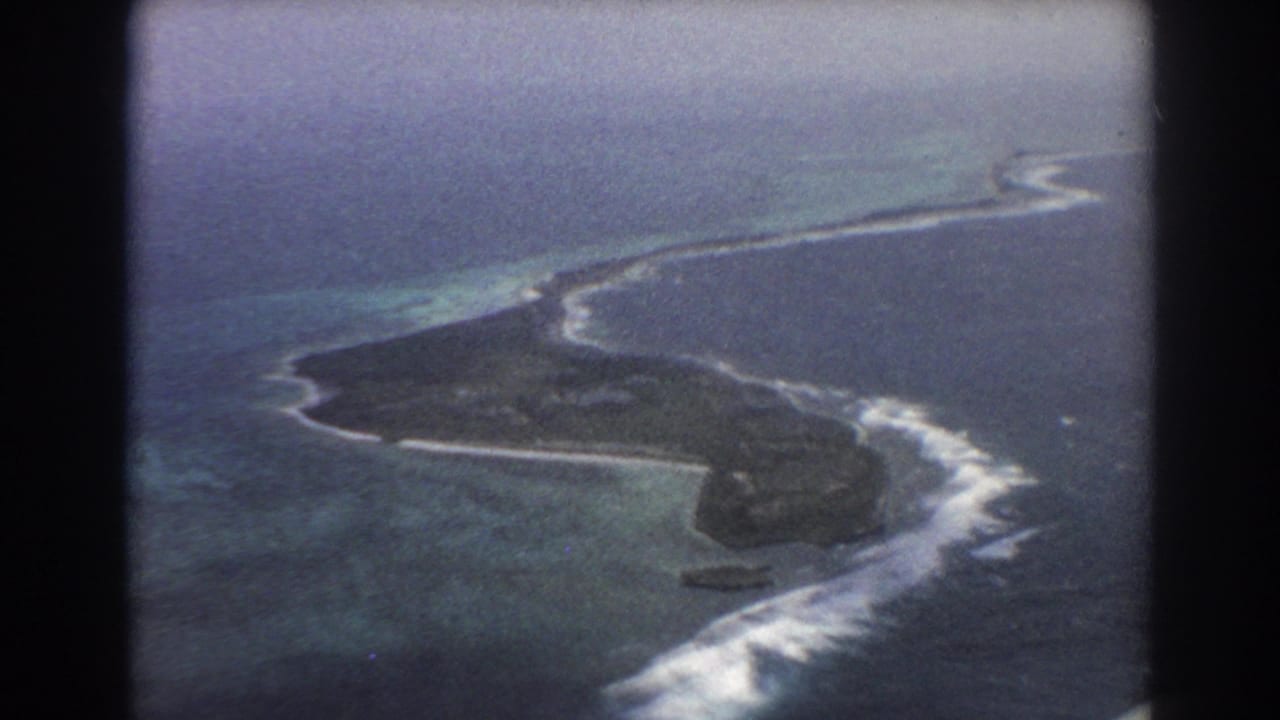 Aerial view of a narrow island surrounded by reef surf and blue-green ocean.