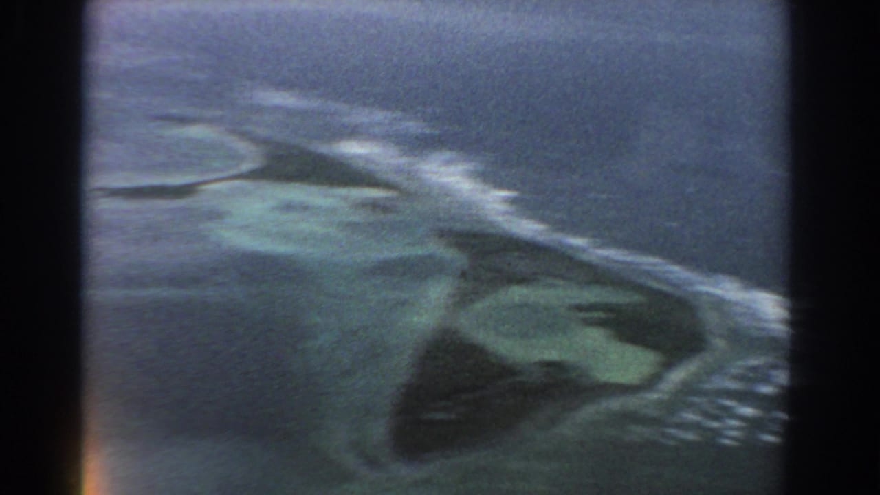 1967 8mm aerial view near Perth, Australia, showing a low island or reef area surrounded by pale surf and blue-green water.