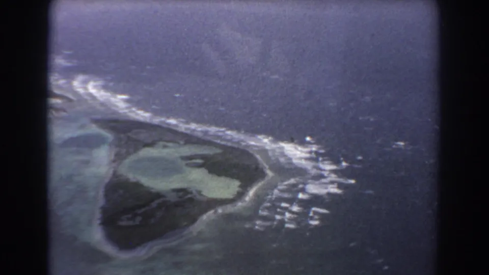 1967 8mm aerial footage appears to show an island shoreline, reef flats, breaking surf, and darker sea beyond near the Australian coast.