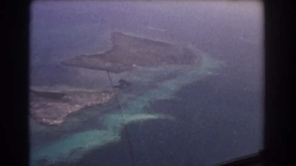 1967 8mm airplane-window view near Perth, Australia, showing reef patterns, shallow blue-green water, and coastline below.