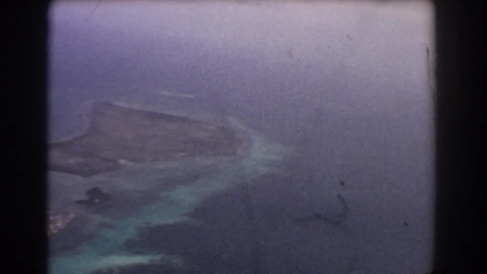 A soft 8mm frame shows reef patches and turquoise shallows through the airplane window during a 1967 Australia flight.