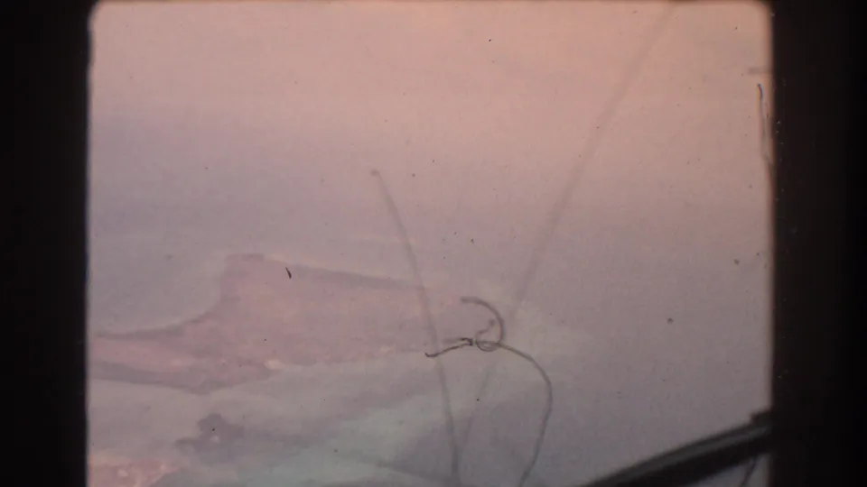 The final 1967 8mm frame is pink and hazy, with faint reef water, coastline, window edge, and visible film debris.