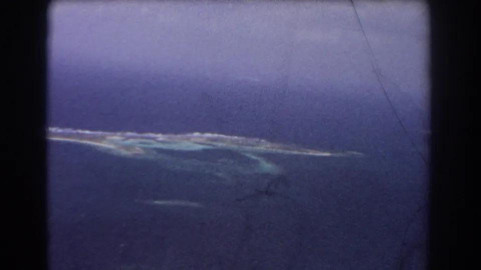 1967 aerial 8mm view of a narrow island chain with pale reef edges and turquoise shallows in deep blue water near Perth, Australia.