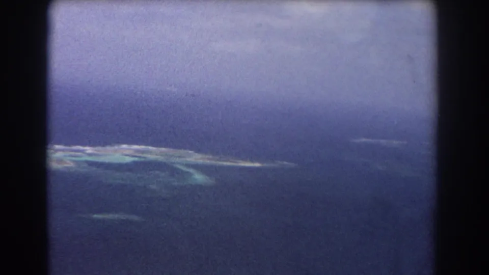 1967 8mm aerial frame showing an island reef system and blue ocean during a slow airborne pan near Perth, Australia.