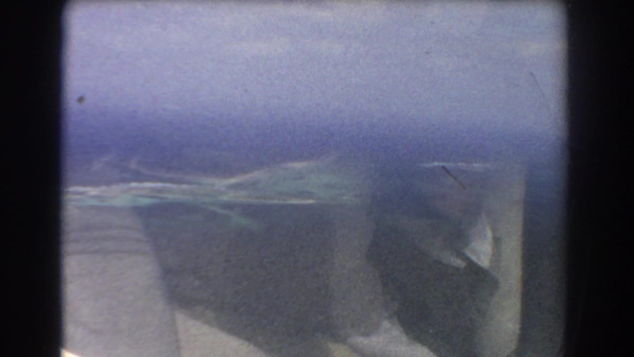 Blurred airplane-window view of sea and a small island or reef below.