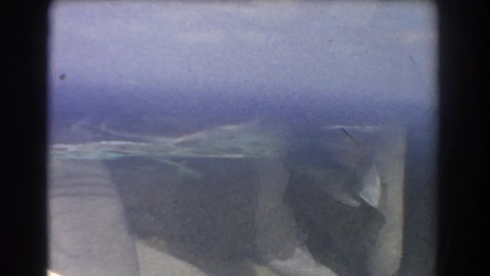 1967 8mm-style airplane-window view near Perth metadata, with a soft blue sea surface and small island or reef shape below.