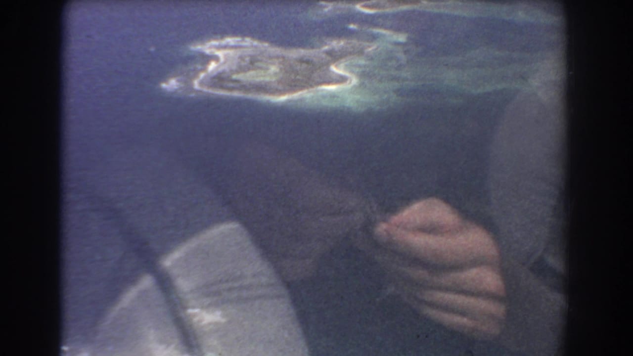 Small island seen through an airplane window with a reflected hand holding a cigarette.