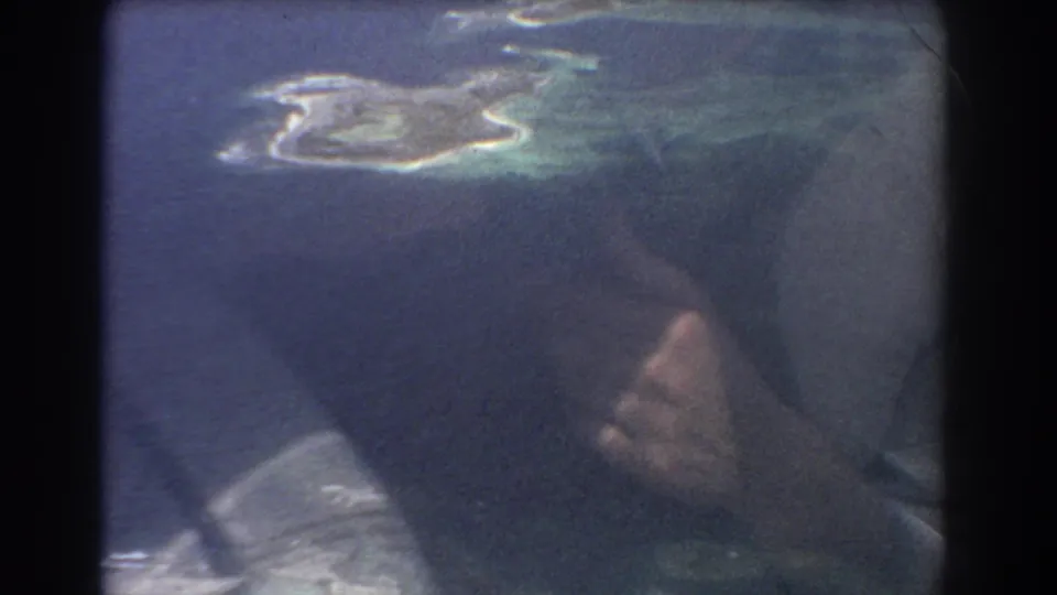 Aerial island view through an airplane window, with reflected hands visible in the glass during a 1967 Australia home-movie shot.