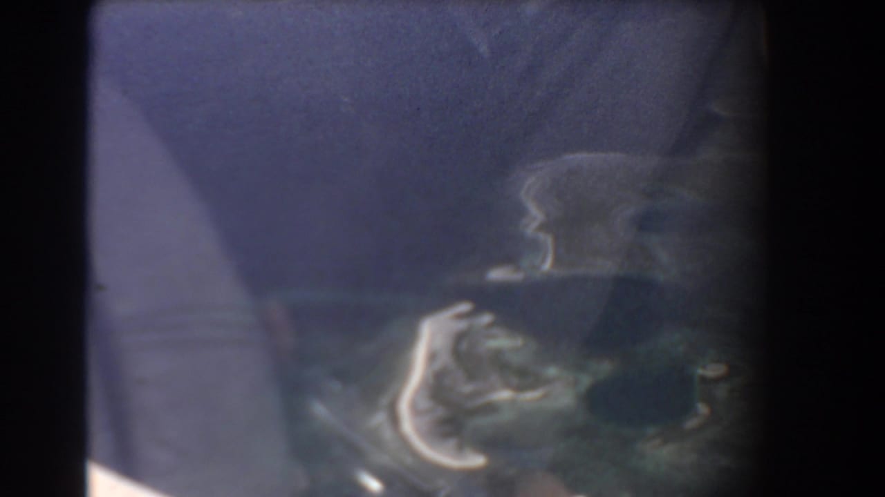 Dark aircraft window frame with a soft blue aerial view and faint coastline below.