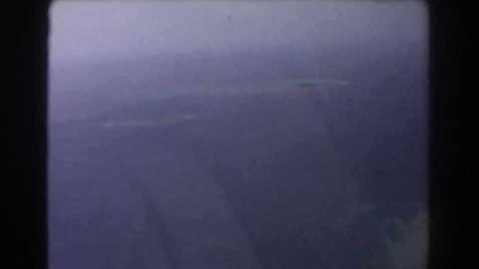 1967 Perth-area 8mm aerial view with hazy sea and a faint dark coastal landform near the lower edge.