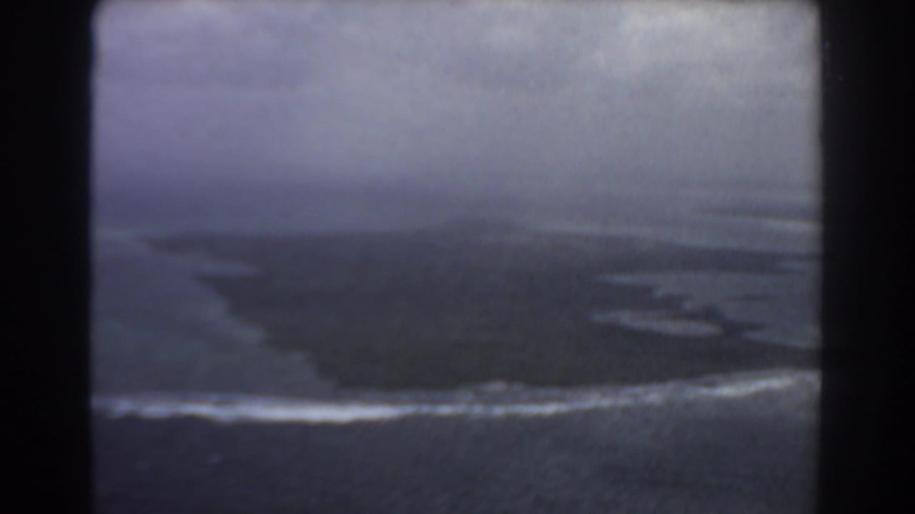 Aerial view of a dark island edge with white surf breaking along the shore.