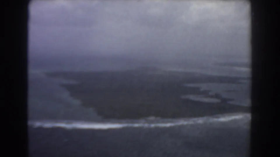 1967 Perth-area aerial frame showing a dark island or coastal point bordered by white surf and muted sea.