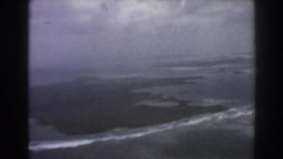 1967 Perth-area 8mm frame showing a small dark landform ringed by pale surf in blue-gray water.