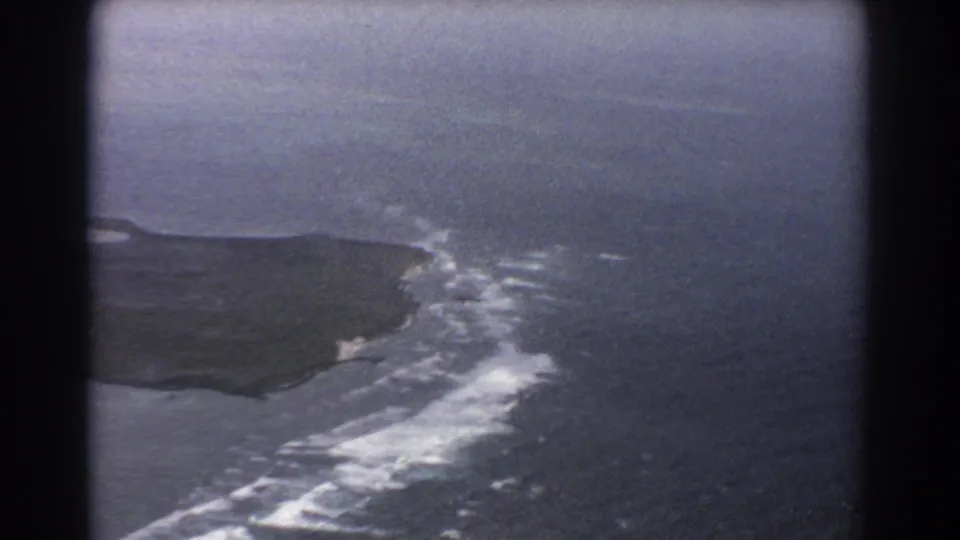 1967 8mm aerial view near Perth, Australia, showing a rugged island edge bordered by white surf and open ocean.