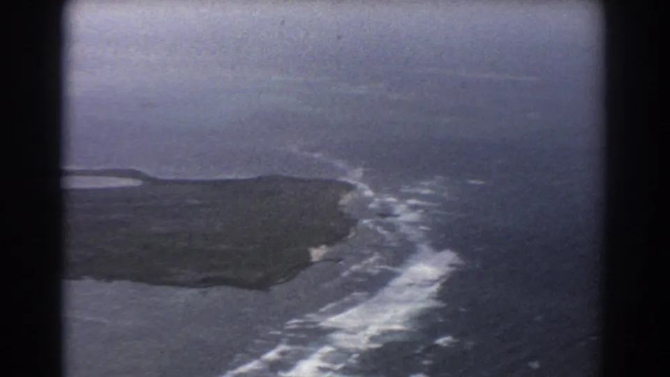 1967 home-movie aerial footage near Perth, Australia, with a dark coastal landmass and foaming surf patterns offshore.