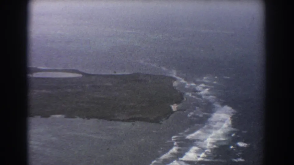 1967 8mm aerial footage near Perth, Australia, with rugged coastline, white wave breaks, and a hazy ocean distance.