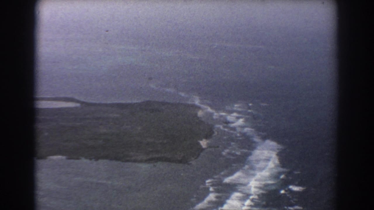 Aerial view of coastline and surf seen through a dark airplane-window frame.