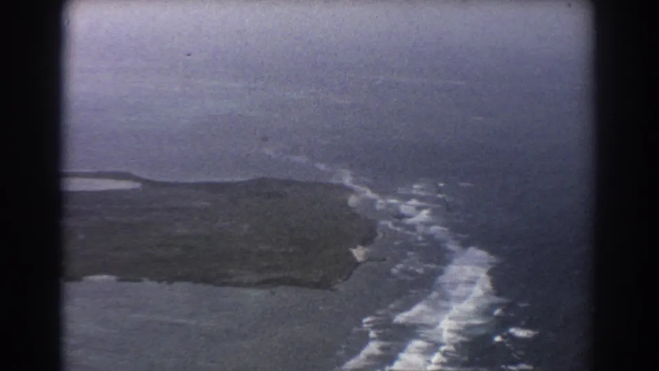 1967 8mm aerial view near Perth showing a rugged coast, white surf, open ocean, and dark window or film-gate edges.