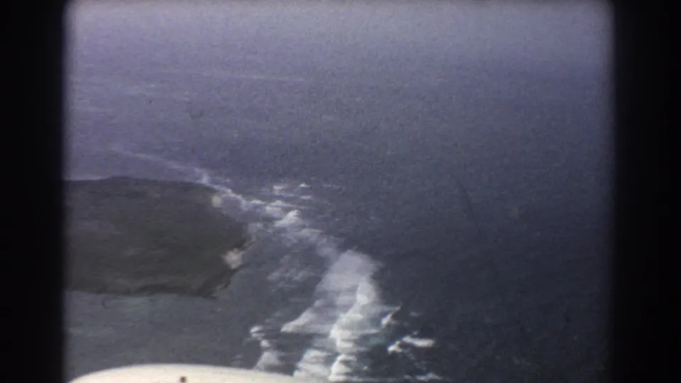 Aerial 8mm frame near Perth with a headland, surf line, blue-gray ocean, and rounded airplane-window or film-frame edges.