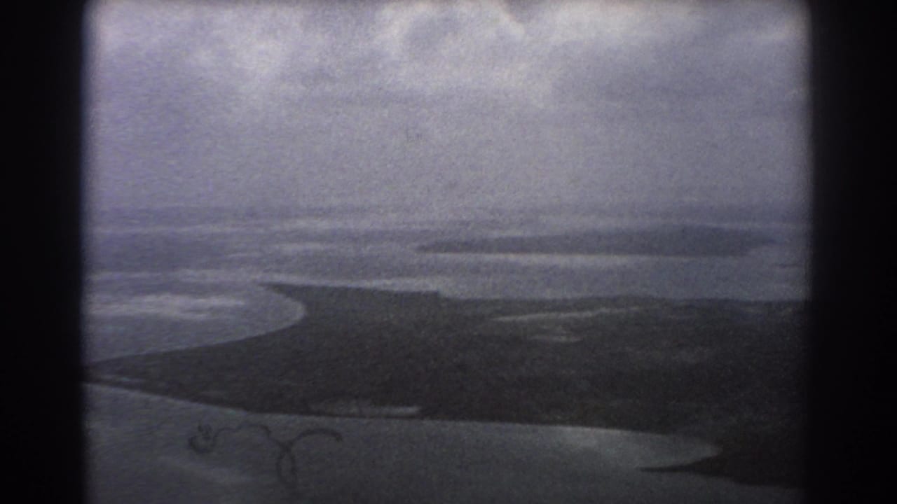 Aerial coastal view with a dark island shape, surrounding water, and heavy window framing.